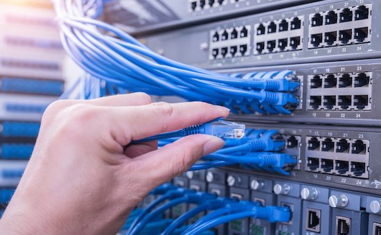 A man connecting cables into an IT network switch in the Okanagan